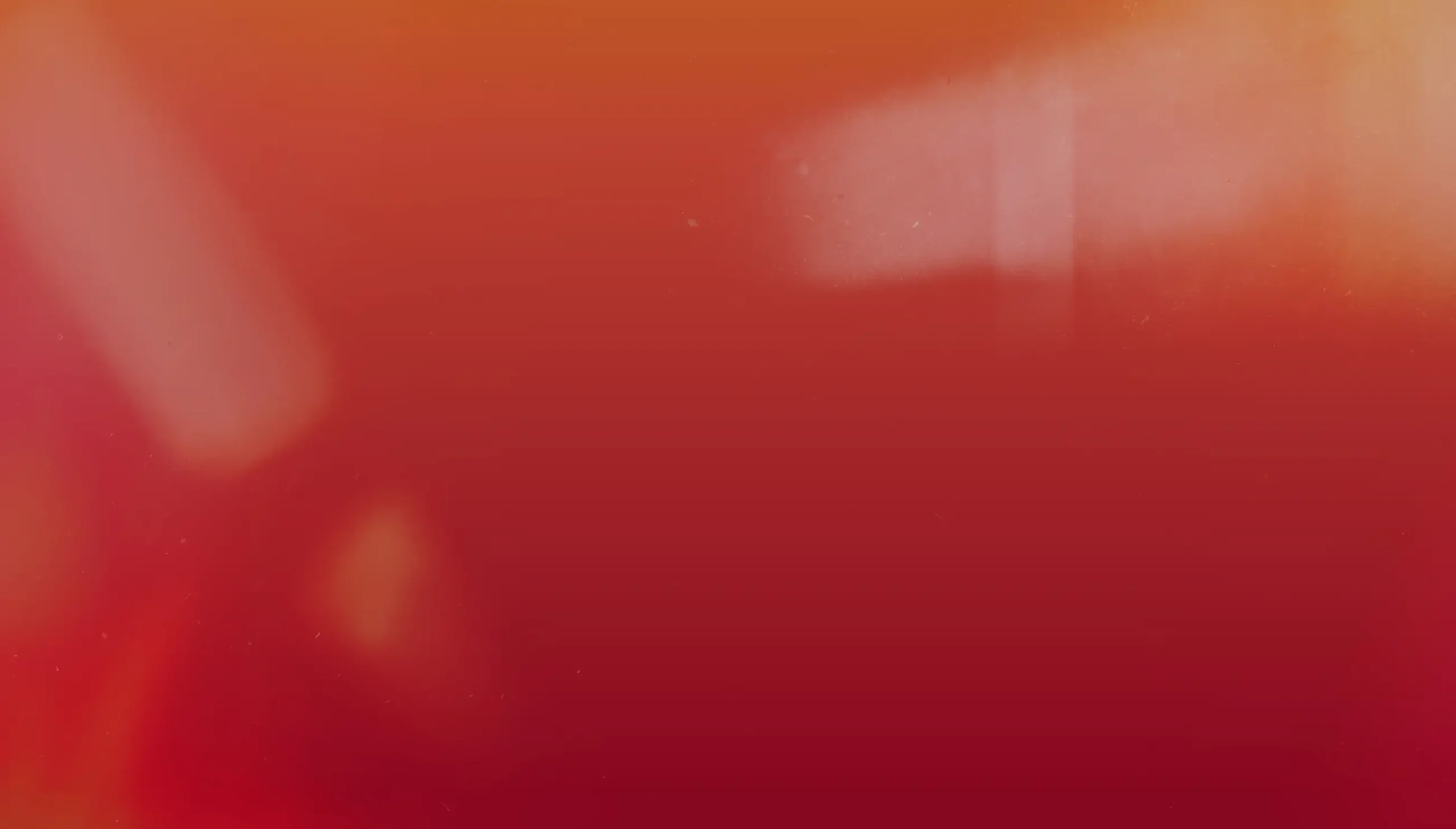 A warm gradient background transitions from deep red at the bottom to a soft orange at the top. Light, blurred shapes are visible, creating a dreamy, abstract effect.