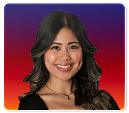 A woman with long, wavy dark hair and highlights smiles at the camera. She wears a black top and a necklace with a "K" pendant. The background is a gradient of purple, red, and orange.