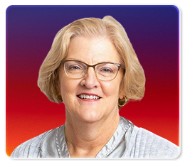 A smiling older woman with short blonde hair, glasses, and a light gray blouse, posed in front of a gradient background transitioning from purple at the top to red at the bottom.