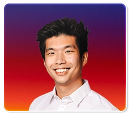 A smiling man with short, dark hair wearing a white collared shirt, posed in front of a vibrant gradient background transitioning from purple at the top to red and orange at the bottom.